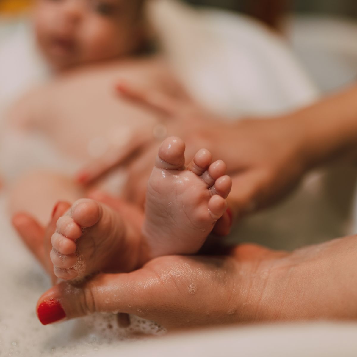 A parent gently bathing a baby, holding the baby's feet