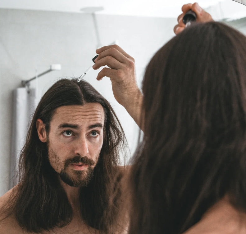 Man with long hair looking at himself in the mirror while using the octaskin serum product.